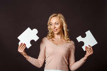 happy blonde woman holding jigsaw pieces isolated on blackの写真素材