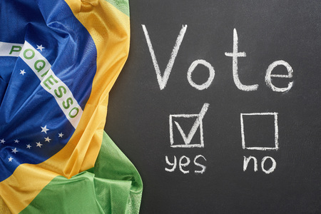 Top view of white vote lettering and check mark near yes word on black chalkboard near flag of Brazilの写真素材