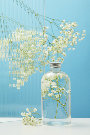 White wildflowers behind textured glass near organic beauty product in bottle on blue backgroundの写真素材