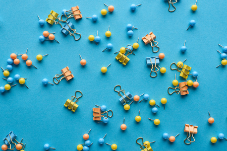Top view of colorful scattered push pins and paper clips isolated on blue background