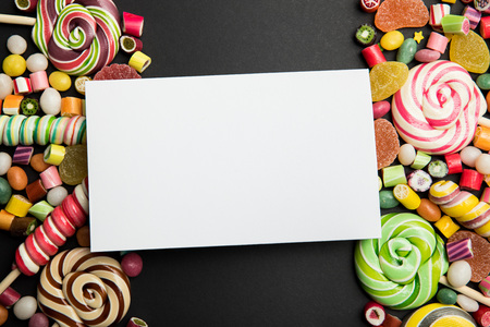 Top view of delicious multicolored sweets and blank white card on black backgroundの写真素材