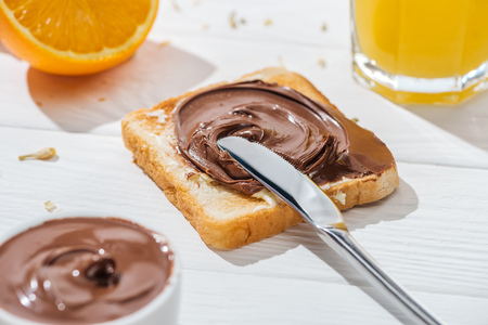 Selective focus of toast with chocolate cream near knife and half of orange on white backgroundの写真素材