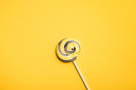 Top view of delicious multicolored swirl lollipop on wooden stick on yellow backgroundの写真素材