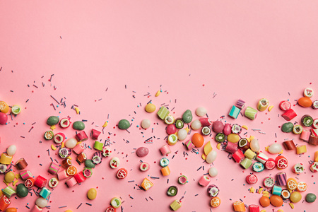 Top view of colorful tasty candies and sprinkles scattered on pink background with copy spaceの写真素材