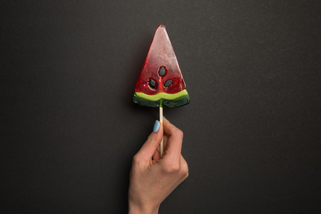 Cropped view of woman holding watermelon tasty lollipop on black backgroundの写真素材