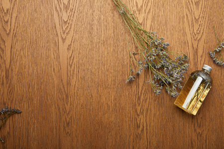 Top view of transparent bottle with organic beauty product near dried herbs on wooden backgroundの写真素材