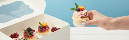 Panoramic shot of woman holding cupcake with fruits and cream isolated on blue backgroundの写真素材
