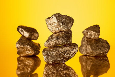 S elective focus of three stacks of gold shiny stones with reflection isolated on yellow backgroundの写真素材