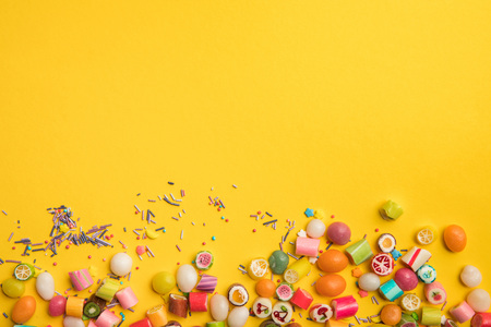 Top view of multicolored tasty candies and sprinkles scattered on yellow background with copy spaceの写真素材