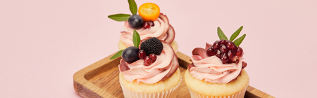 Panoramic shot of cupcakes with fruits and berries on wooden tray isolated on pink backgroundの写真素材