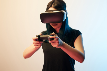 Young woman playing video game while wearing virtual reality headset on beige and blue background