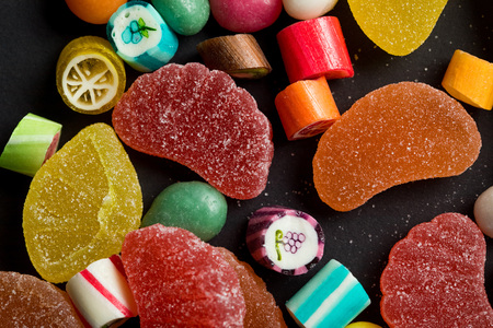 Close up view of caramel multicolored candies and sugary fruit jellies on black background