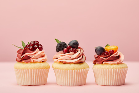 Sweet cupcakes with fruits and berries on pink surfaceの写真素材