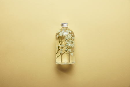 Top view of bottle with organic beauty product and dried white wildflowers inside on yellow backgroundの写真素材