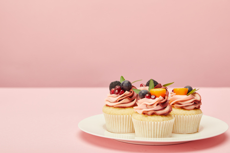 Sweet cupcakes with berries and fruits on plate on pink surfaceの写真素材