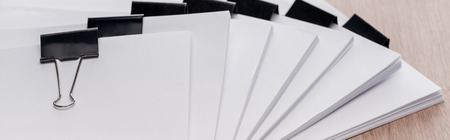 Panoramic shot of stacks of blank paper with metal binder clips on table