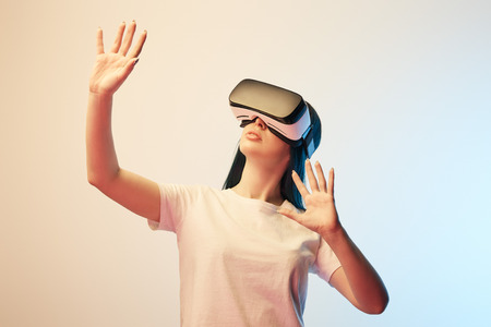 Young woman in virtual reality headset gesturing on beige and blue backgroundの写真素材