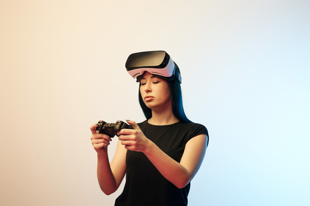 Young woman looking at joystick while wearing virtual reality headset on beige and blue background