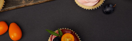Panoramic shot of cupcakes with kumquats on black surface