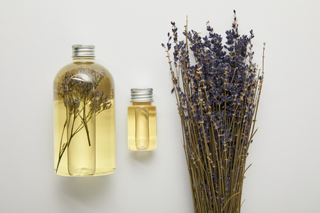 Top view of transparent bottles with natural liquid yellow beauty products near dry purple wildflowers on grey backgroundの写真素材