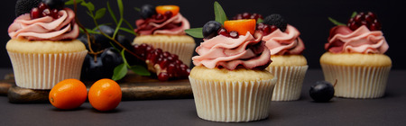 Panoramic shot of cupcakes with cream, fruits and berries isolated on black background