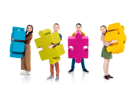 happy kids looking at camera and holding jigsaw puzzle pieces on whiteの写真素材