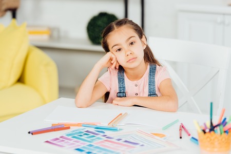 selective focus of upset kid looking at camera near papers with drawing