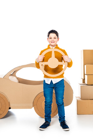 boy near cardboard car holding steering wheel and looking at camera on whiteの写真素材