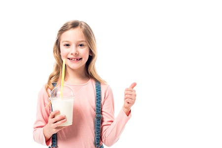 Smiling kid holding milkshake and showing thumb up isolated on white backgroundの写真素材
