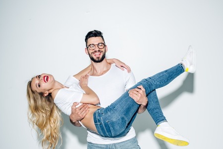 Happy man in glasses holding in arms attractive blonde girl on white backgroundの写真素材
