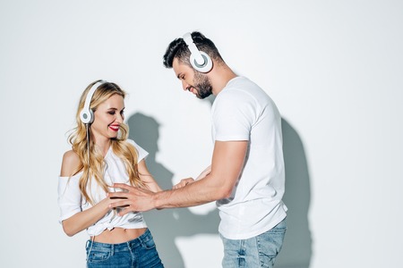 Happy man in headphones touching cheerful blonde girl on white backgroundの写真素材