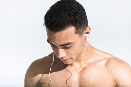 handsome shirtless mixed race man listening music in earphones on whiteの写真素材