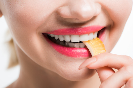 cropped view of smiling woman eating orange jelly candy isolated on white