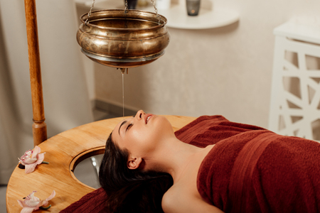 relaxed young woman lying under shirodhara vessel during ayurvedic procedureの写真素材