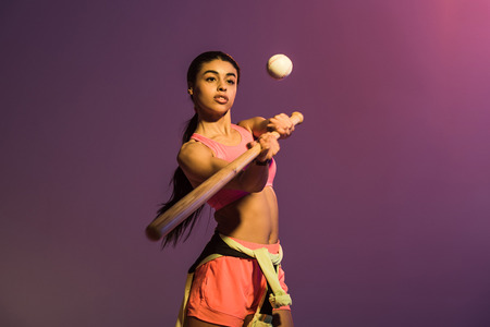 attractive sportive african american girl playing baseball on purple backgroundの写真素材