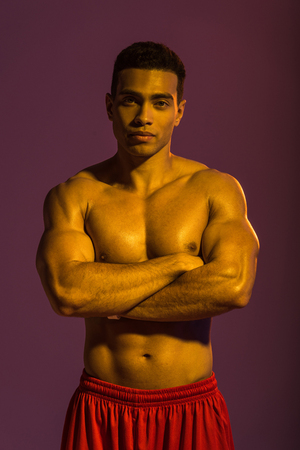handsome sportive mixed race man posing at camera with crossed arms on purple backgroundの写真素材