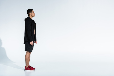 side view of sportive mixed race man in black sportswear and red sneakers on white background with copy spaceの写真素材