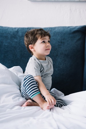 cute kid sitting on bed with white bedding at homeの写真素材