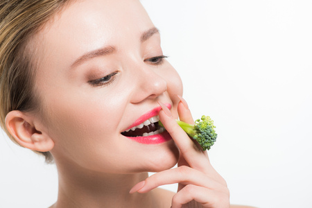 attractive and happy woman eating green ripe broccoli isolated on whiteの写真素材