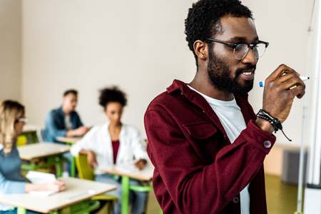 smiling african american student in glasses writing on flipchartの写真素材