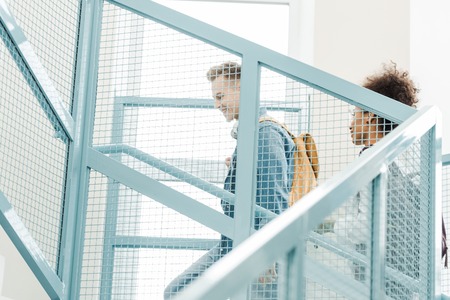 two multicultural students with backpacks on stairs in universityの写真素材