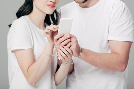 partial view of man and woman with usb cable around hands using smartphone isolated on greyの写真素材