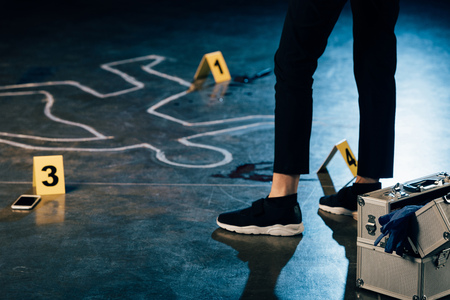 partial view of investigator standing near chalk outline and evidence markers at crime sceneの写真素材