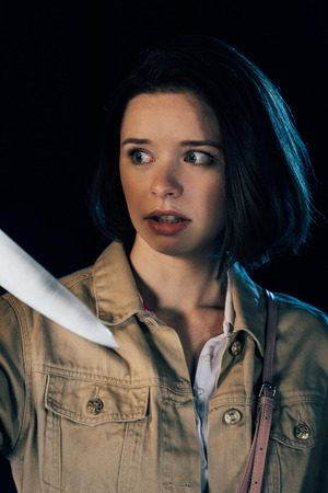 pretty scared woman looking at knife isolated on blackの写真素材