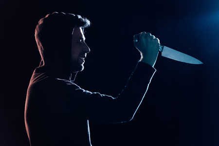 side view of smiling criminal in casual clothes holding knife on blackの写真素材