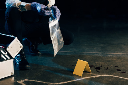 cropped view of investigator in uniform with evidence at crime sceneの写真素材