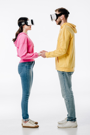 young man in woman in blue jeans and hoodies holding hands while using virtual reality headsets on white backgroundの写真素材