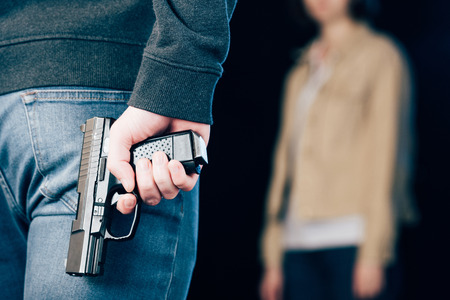 cropped view of criminal hiding gun while standing near woman on blackの写真素材
