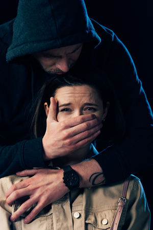 partial view of criminal attacking scared woman and covering her mouth isolated on blackの写真素材