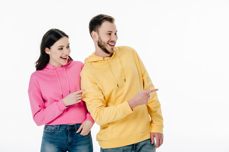 young cheerful man and woman in hoodies looking away and pointing with fingers isolated on whiteの写真素材